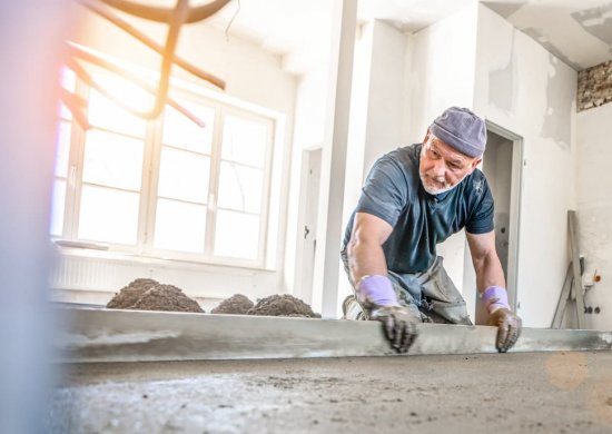 BRW | Baufinanzierung | Arbeiter, der den Hausboden mit Zement begradigt